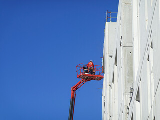 Lone worker in mid air with a blue sky and red nacelle. France.