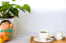 Coffee On A Wooden Tray Is Placed On A Table With White Background. There Are Decorative Pots And Ceramic Dolls On The Side.