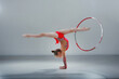 Image of flexible little girl doing exercise on hands with hula hoop in pink sportwear in gray studio