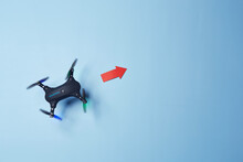 Aerial Top Down View On Isolated Drone Copter With Spinning Propellers Flying In The Red Arrow Direction Above The Bright Solid Blue Fond Background