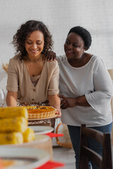 Wall Mural - African american woman hugging daughter with tasty pie during thanksgiving celebration