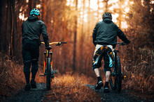 Two Mountain Bikers Pushing Their Bike Through An Autumn Forest