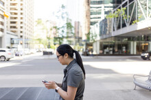 Woman Using Phone On Sidewalk In City Center
