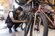 Young Owner On Phone, Checking Bicycle Wheel In Sports Store