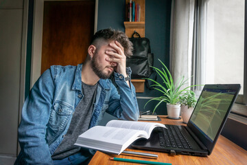 young college student tired of studying from a book and laptop