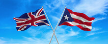 Flags Of Great Britain And Puerto Rico Waving In The Wind On Flagpoles Against Sky With Clouds On Sunny Day. Symbolizing Relationship, Dialog Between Two Countries. 3d Illustration
