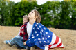 © Надежда Урюпина - brother and sister on the shore, wrapped in an American flag, happy laughing children, a girl and a boy, the concept of patriotism and the celebration of US independence. US Veterans Day