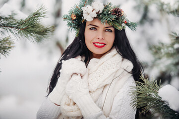 Wall Mural - Portrait of a woman in white clothes in a cold winter forest. Girl with a wreath on her head in a snow-covered winter forest