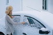 Caucasian young girl cleaning car from snow near the house