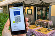 Woman showing on smartphone EU Digital Covid Certificate Green Pass with quad code. Restaurant background.