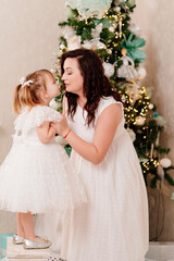 mother and daughter in white dresses at home at the Christmas tree.