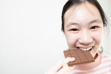 Asian teenage lady girl eating tasty chocolate bar,deliciously sweet,enjoy the natural taste,happy young woman holding chocolate bar,biting a bar of chocolate made from roasted and ground cacao seeds