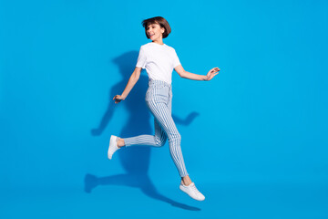 Wall Mural - Photo of cute shiny young woman dressed casual clothes running looking back empty space smiling isolated blue color background