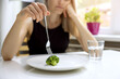 Leinwandbild Motiv dieting problems, eating disorder - unhappy woman looking at small broccoli portion on the plate