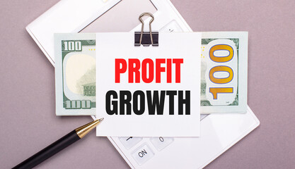 Fototapete - On a gray background, a white calculator, a pen, banknotes and a sheet of paper under a black paper clip with the text PROFIT GROWTH. Business concept