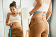 Leinwandbild Motiv Reflection in mirror of happy woman measures her slim waist with tape measure.