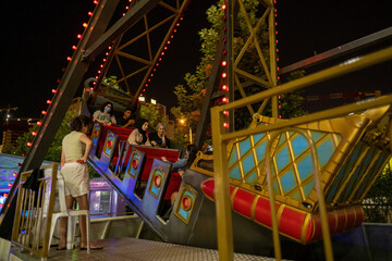 Maltepe, Istanbul, Turkey - 07.22.2021: several Turkish people on swinging pirate ship amusement park ride at night time in a summer day for entertainment having fun leisure time togetherness concepts