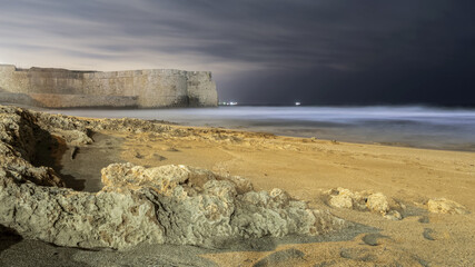 Wall Mural - Scenic shot of the beach of the sea surrounded by mountains on a dark rainy day