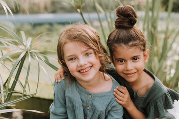 Portrait of two charming smiling girls belonging to different races surrounded by tropical leaves. Friendship, linen clothing, environmental friendliness. High quality photo