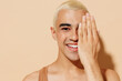 Close up young smiling latin gay man with make up in beige tank shirt hug himself look camera cover half face with hand isolated on plain light ocher background studio People lgbt lifestyle concept