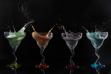 Cocktail glasses with colorful alcoholic drinks splashing on a black background