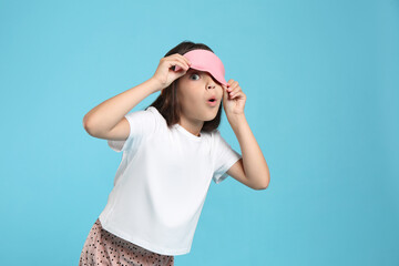 Wall Mural - Cute girl wearing pajamas and sleeping mask on light blue background