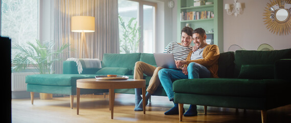 Portrait of Gentle Gay Couple Using Laptop Computer, while Sitting on a Couch in Cozy Stylish Apartment. Adult Boyfriends Online Shopping on Internet, Watching Funny Videos on Streaming Service.