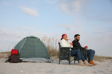 Wall Mural - Couple with hot drinks near camping tent on beach