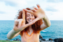 Smiling Woman Showing Triangle Gesture Near Sea Coast