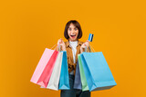 Fototapeta Mapy - Sales and discounts concept. Excited woman holding credit card and colorful shopping bags, yellow background