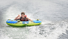 Happy Teenager Having Fun On A Tube Pulled By A Boat On A Lake.