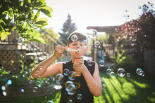 Young Boy Blowing Bubbles In A Backyard On A Sunny Day.