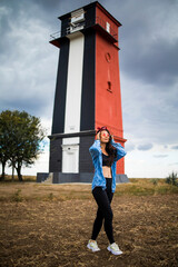 Wall Mural - Asian woman sightseeing lighthouse seascape in europe travel outdoor recreation lifestyle concept. girl hair in the wind wearing a denim jacket