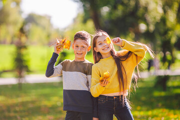 Friendship between siblings. Siblings together outside with bright colored background. Kids autumn portrait. Brother and sister playing in autumn park leaves. Family active fall weekend concept