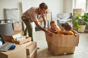 Wall Mural - Portrait of modern father playing with two boys in cardboard box while family moving to new house, copy space