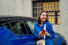 Beautiful Woman Next To Blue Car Using And Looking At Cell Phone