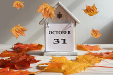 Calendar For October 31 : Decorative House With Numbers 31 And The Name Of The Month In English, Falling Maple Leaves, Gray Background, Side View