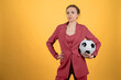 Beautiful young woman businesswoman with soccer ball posing on yellow background
