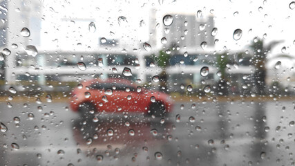 Sticker - Closeup shot of the surface of a mirror with raindrops against a blurred red car background