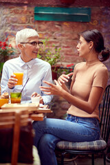 vertical image of young adult female talking to an elderly woman explaining something to her, while having breakfast together