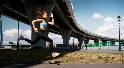 Wall Mural - The athlete leads a healthy lifestyle. Cardio training for weight loss. Sports and clothing for women. Fitness in the city. A professional trainer does warm-up exercises before training.