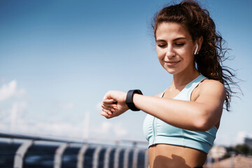 Sports and clothing for women. The calorie counting coach looks at the smartwatch. Fitness break in the city. The athlete leads a healthy lifestyle. Cardio training for weight loss.