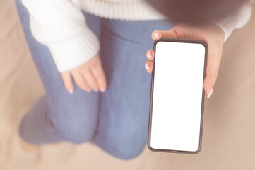 Wall Mural - woman or teen girl hands holding cell phone mockup white blank display, empty screen for social media app ad at home. Female hands using smartphone in blurred background