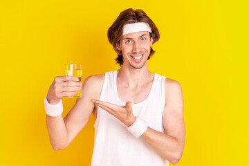 Sticker - Portrait of attractive sportive cheerful guy drinking demonstrating water isolated over shine yellow color background