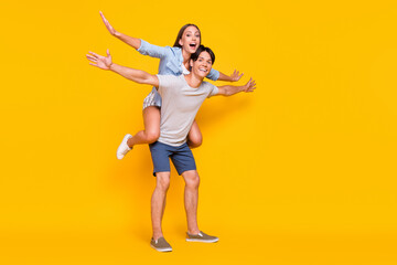 Canvas Print - Full length body size view of attractive cheery couple piggy backing summertime jet isolated vivid yellow color background