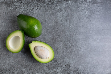 two green avocados lie on an artificial stone board. diet food. green vegetable.avocado cutaway. avocado seed. space for design and for text