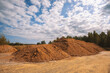 Large pile of industrial sand, stockpiled and prepared for use in construction and road construction, against a backdrop of blue sky and green forest
