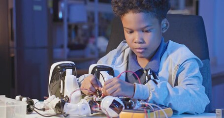 Young african american boy repairing a robotic toy at home. Smart kid assembling and testing electric circuit building and programming robot. People with futeristic technology and education concept.