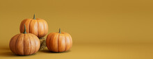 Three Pumpkins On A Mustard Yellow Colored Background. Fall Themed Banner With Copy-space.