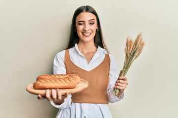 Wall Mural - Beautiful brunette young woman holding homemade bread and spike wheat winking looking at the camera with sexy expression, cheerful and happy face.